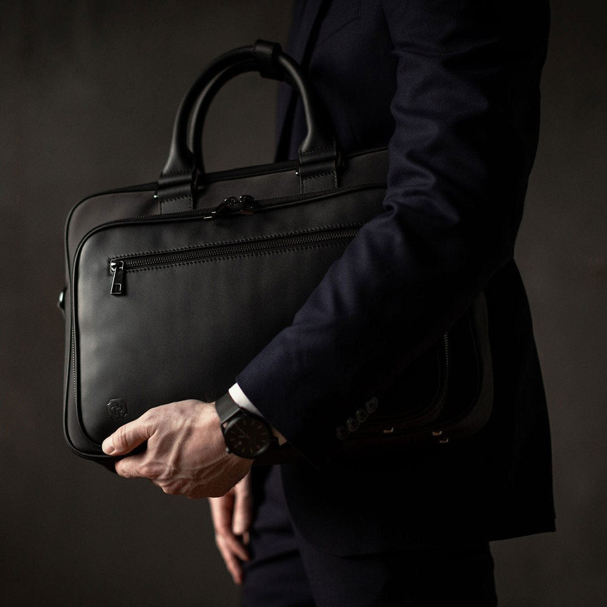 A hand holding the black Alto by its full-grain leather handles